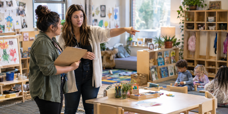 Two daycare educators discussing classroom responsibilities in a preschool learning environment
