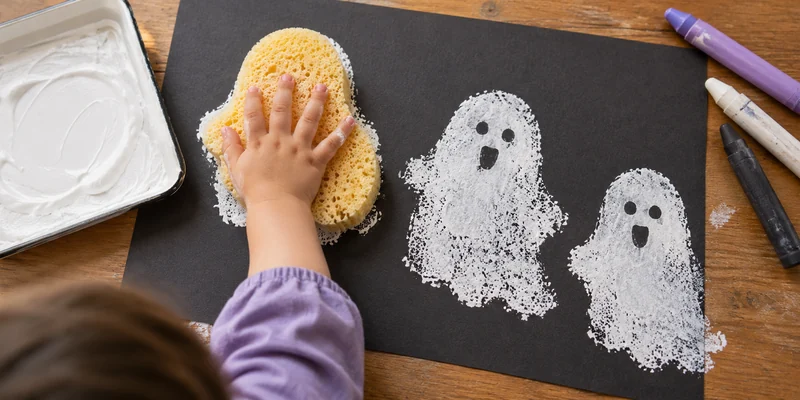 Child making white ghost prints on dark paper with a large sponge